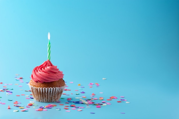 Pink birthday cupcake with green candle on blue background