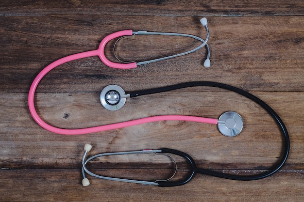 Pink and black Stethoscope on wood table.