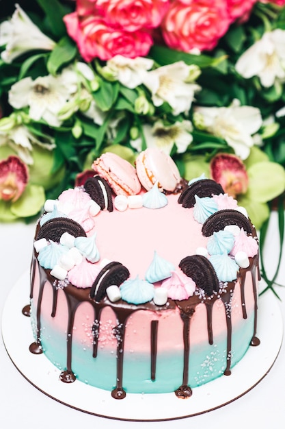 Pink and blue cake decorated with cookies, meringues and macaroons, with smudges of chocolate coating.