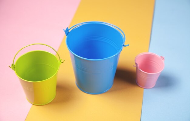 Pink, blue, green bucket on the color paper surface.