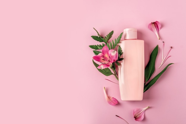 Pink bottle with moisturizer on pink background with flowers Alstroemeria. Cosmetic container mockup with place for text. Natural skincare beauty product concept.