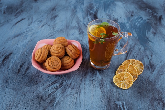 Pink bowl of mini cinnamon cakes with glass of tea on stone surface