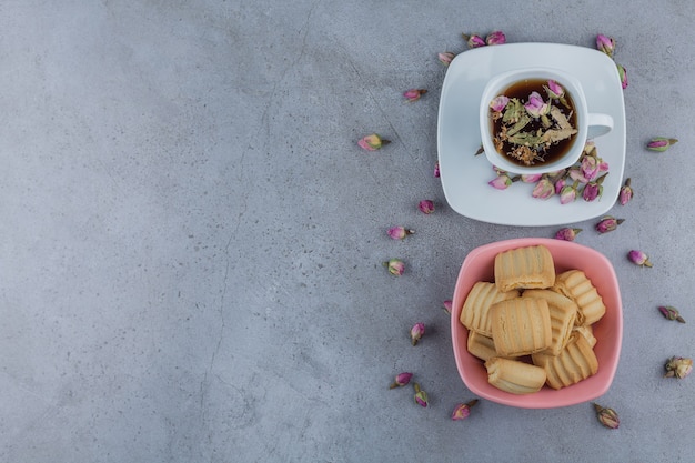 Pink bowl of sweet biscuits and cup of hot tea on stone.