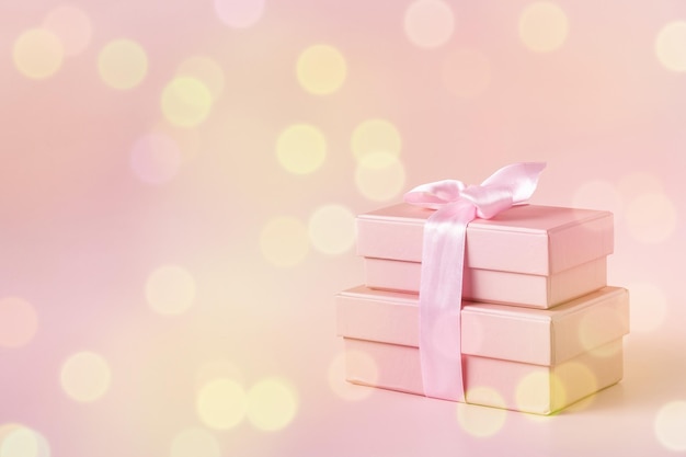 Pink boxes with gifts tied with ribbons on a pink background\
with bokeh copy space