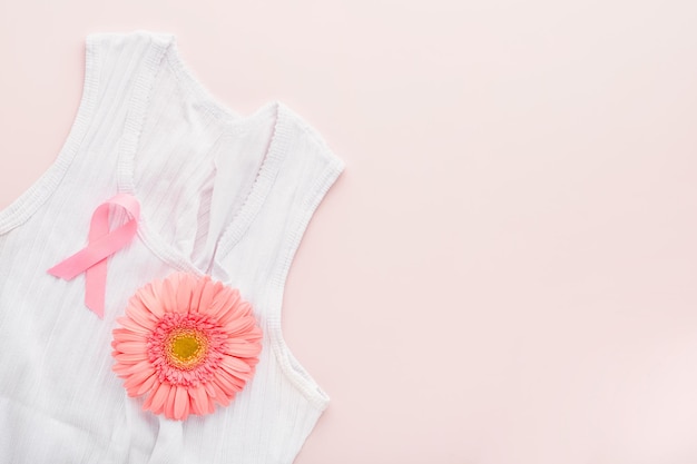 Pink Breast Cancer Awareness Ribbon Gerbera and pink ribbon tape lying on female white tshirt on backgrounds Breast cancer awareness and October Pink day world cancer day Top view Mock up