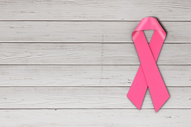 Photo pink breast cancer awareness symbol ribbon on a wooden table background. 3d rendering