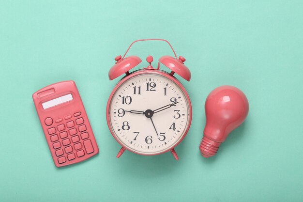 Pink calculator and alarm clock light bulb on mint green background Minimalism Creative layout Fresh idea Top view Flat lay