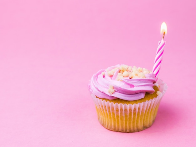 Photo pink candle in berry cupcake on pink surface