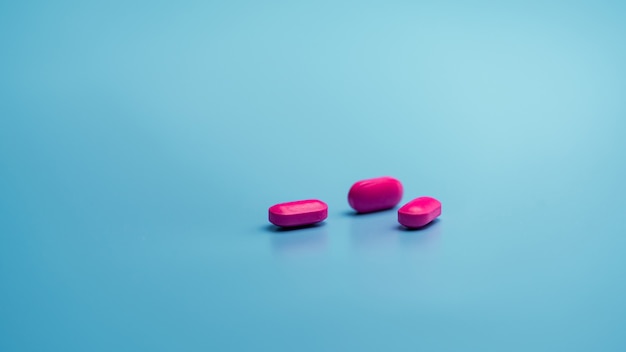 Pink capsule pills on blue background. Pharmaceutical industry. Health and medicine.