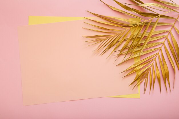 Pink card copy space for text in frame made of Golden palm leaf. Tropical palm leave on pink background. Painted gold leave. Summer floral background.