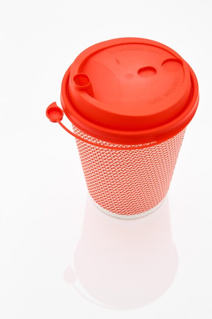 The pink cardboard coffee cup with a red plastic lid on the white glossy background the inscription