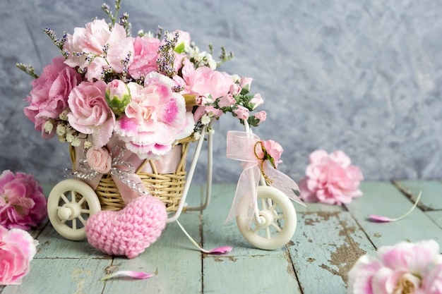 Pink carnation in bicycle with pink knitting wool heart on old wood 