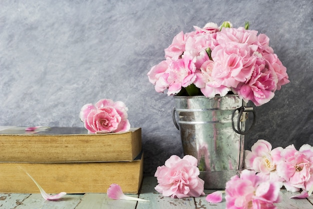 Pink carnation flowers in zinc bucket and old book on table wood