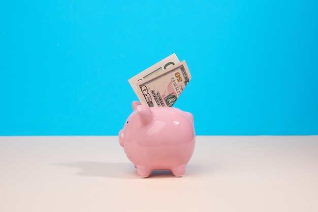 Photo pink ceramic piggy bank with paper us dollars on a blue backgrou