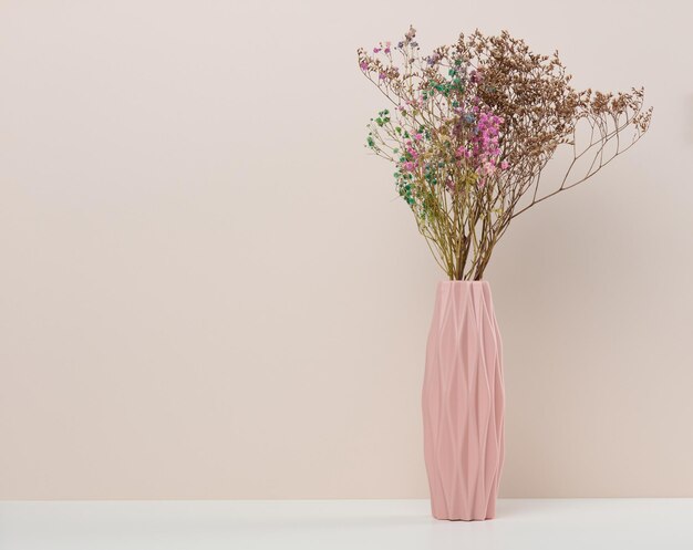 Pink ceramic vase with dry flowers on a white table