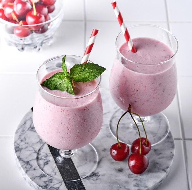 Pink cherry smoothies with fresh red berry, chia seeds, mint green leaves, white stone kitchen background. Selective focus.