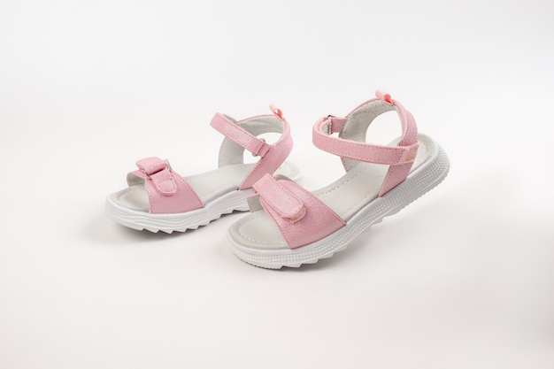 Pink childrens sandals made of shiny leather with velcro fasteners flat white soles isolated on a wh...