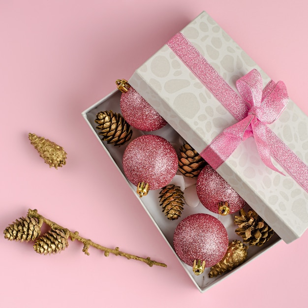 Pink Christmas . Gift box filled with golden cones and baubles.