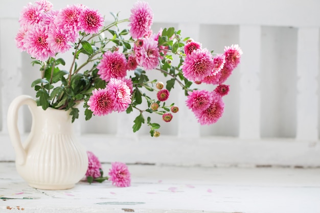 Pink chrysanthemums in jug on old white wood bench