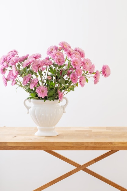 Pink chrysanthemums in white vase on white interior