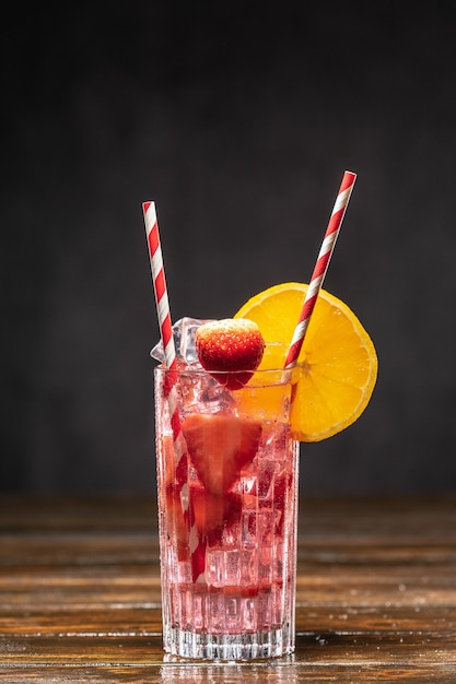 Pink cocktail with ice and strawberries, decorated with orange slice