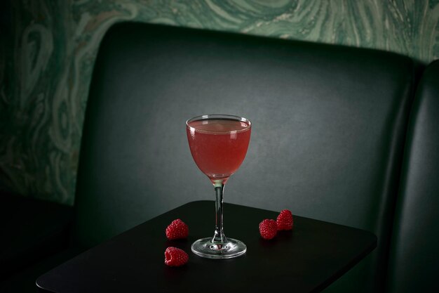 Photo pink cocktail with raspberries in front of green sofa