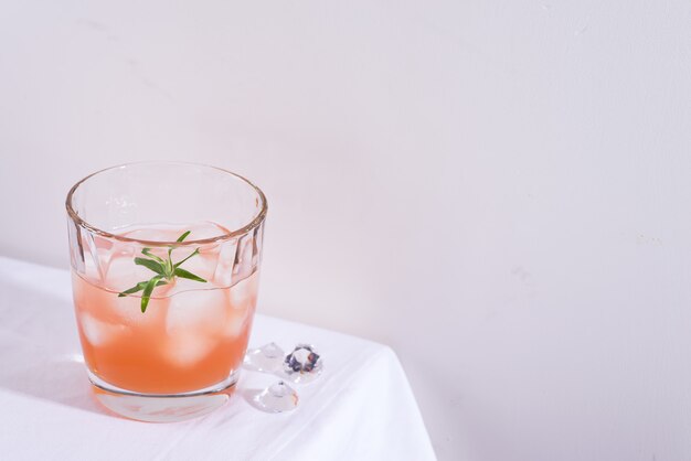 Pink cocktail with rosemary and ice in glass on a white tablecloth on the table