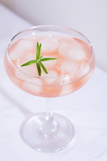 Pink cocktail with rosemary and ice on a white tablecloth on the table