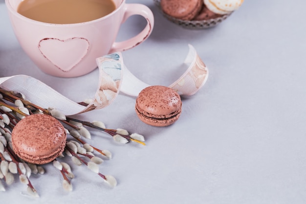 Pink coffee mug with sweet pastel french macaroons and pussy willow on light table from above