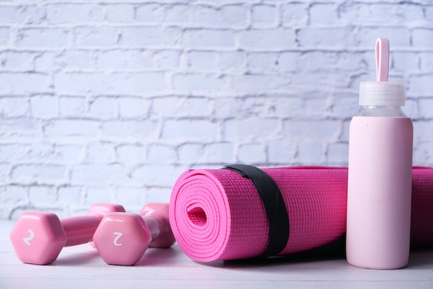 Pink color dumbbell, exercise mat and water bottle on white background .