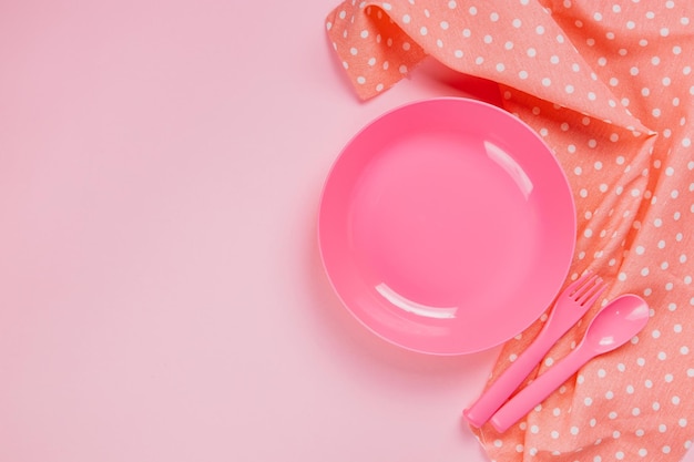 Pink color plastic plate with plastic spoon, fork and pink polka dot Cloth on pink background