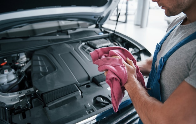 Pink colored towel. Man in blue uniform works with broken car. Making repairings.