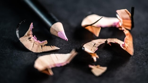 Pink cosmetic pencil with shavings on black background