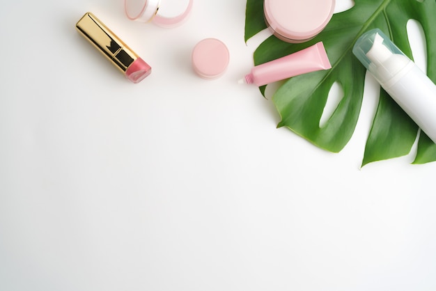 Pink cosmetic products and green leaves on white background