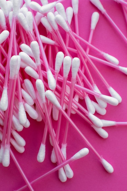 Pink cotton buds with white heads laid out on a pink background