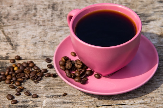 Розовая чашка кофе и кофейных зерен на деревенском деревянном столе
