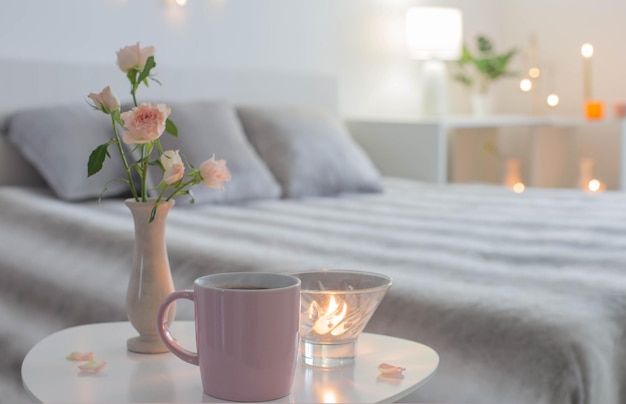 Pink cup of coffee and  roses  in vase on table in bedroom