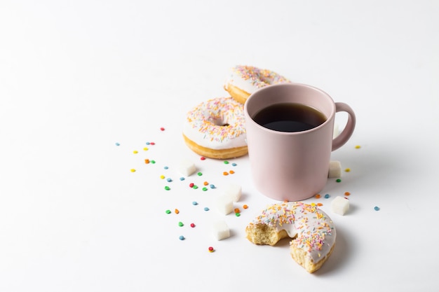 Pink Cup with coffee or tea and fresh tasty donuts, sweet multicolored decorative candy on a white background. Bakery concept, fresh pastries, delicious breakfast, fast food.