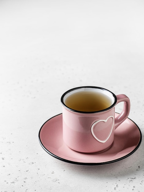 A pink cup with heart of tea standing on a plate on white textured background for St Valentines day