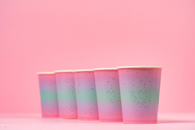 Pink disposable paper cups in a row on pink background