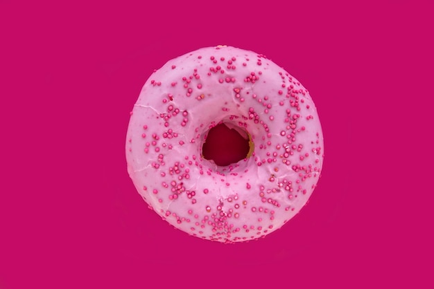 A pink donut with pink frosting and sprinkles on it.