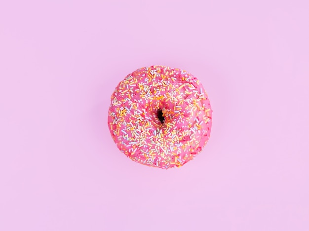 Pink donut with small candies on a pink background