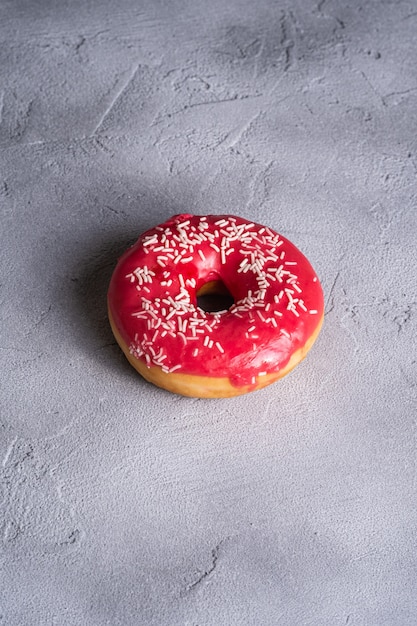 Pink donut with sprinkles, sweet glazed dessert food on concrete textured