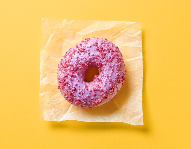 Photo pink donut on yellow paper background, top view