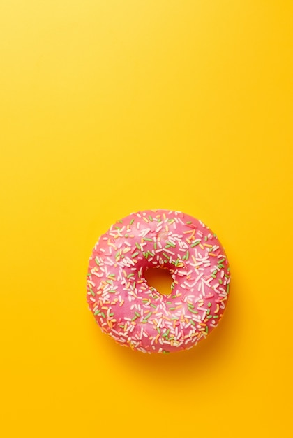 Pink donut on yellow wall top view copy space