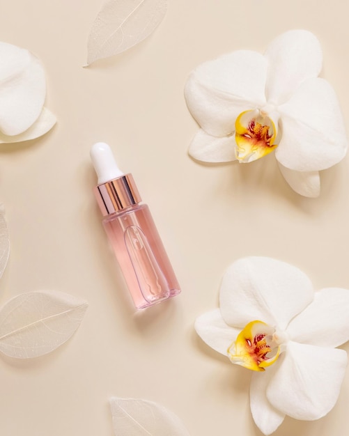 Pink Dropper Bottle near white orchid flowers on light beige top view Skincare beauty product