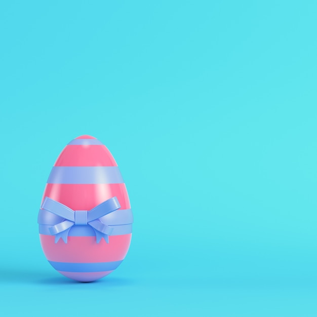 Pink easter egg with bow on bright blue background in pastel colors. Minimalism concept