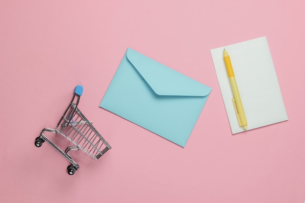 Pink envelope with letter and shopping trolley on pink pastel background. Mockup for valentines day, wedding or birthday. Top view