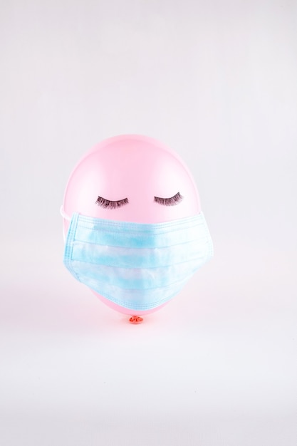 Pink face balloon with black eye lashes closed eyes  with face protective mask. COVID-19 concept.Minimal concept