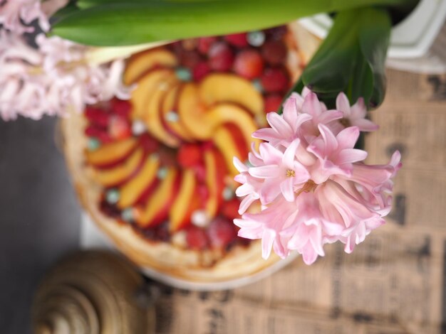 A pink flower is in front of a cake with fruit on it.